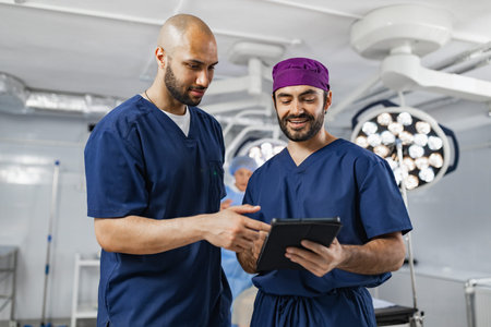 Two surgeons in an operating room review medical records on a tablet, discussing patient care.の写真素材