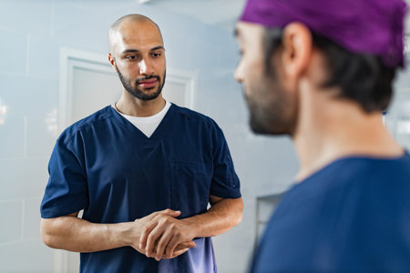 Two surgeons in scrubs converse in a medical setting, likely discussing a procedure or patient care.