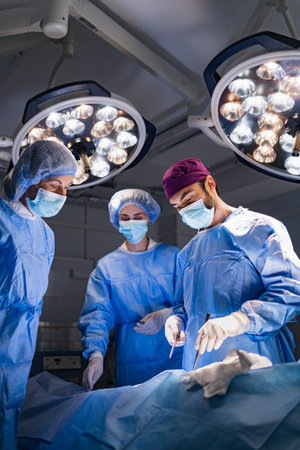 Medical team in surgical gowns and masks operating under bright lights in an operating room.