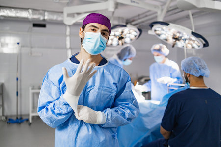 A surgeon wearing a mask and gloves in an operating room, preparing for a procedure with his team in...