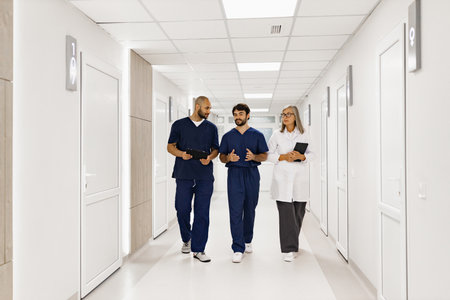 A team of medical professionals, including doctors and nurses, walk and discuss in a bright hospital hallway, likely during rounds or a consultation.の写真素材