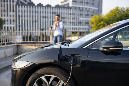 A black electric vehicle is charging, with a man standing in the background.
