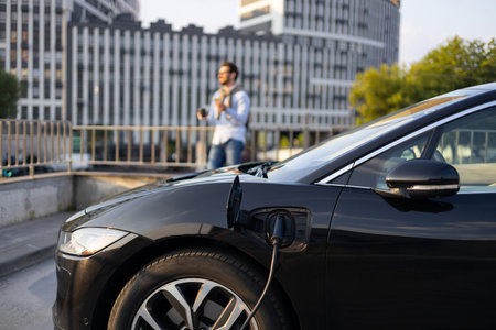 A man waits while his electric vehicle charges in an urban environment, showcasing sustainable...