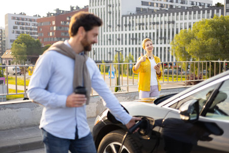 A man charges his electric vehicle while a woman gives a thumbs up in support.