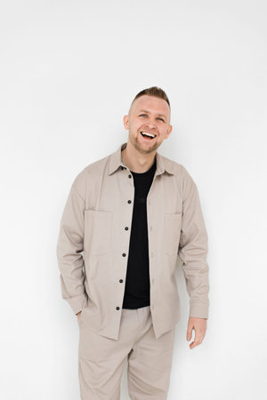 A man with short hair smiles broadly while wearing a beige shirt and pants against a white background.の写真素材