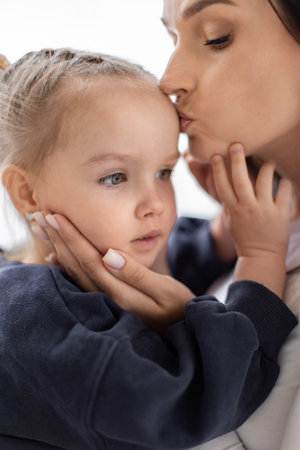 A tender moment between a mother and her young daughter, filled with love and affection. The mother gently kisses her daughters forehead.の写真素材