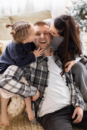 A happy family shares a moment of affection, with a daughter and wife kissing the father.の写真素材