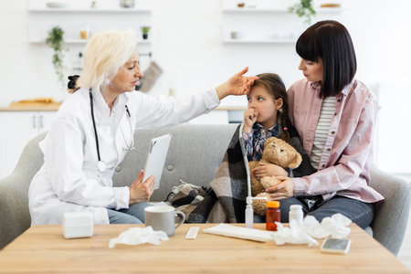 A doctor checks a young girls temperature while the mother comforts her. Medical supplies are on the table.の写真素材