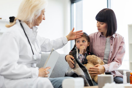 A concerned doctor checks a young girls temperature while the mother comforts her, showing care and concern in a medical setting.の写真素材