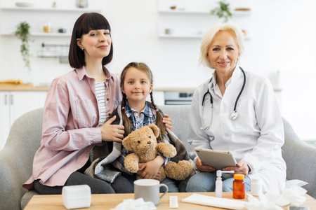 A mother and her daughter are at the doctors office for a checkup. The doctor is smiling and holding...