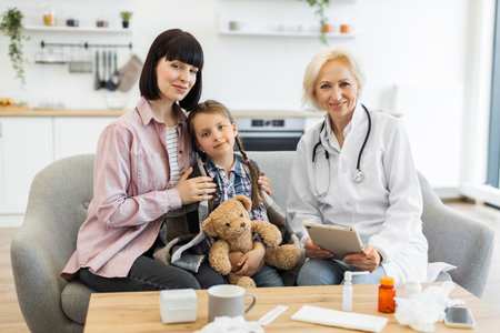 A mother and daughter consult with a doctor in a home setting, with medical supplies on the table.の写真素材