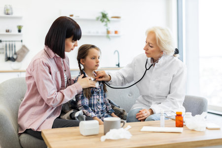 A doctor uses a stethoscope to examine a young girl while her mother sits beside her, providing comfort and support during the checkup.の写真素材