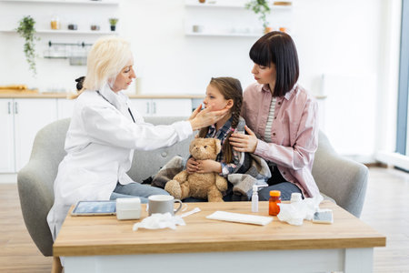 A doctor checks a childs throat while the mother comforts her. The scene takes place in a living...