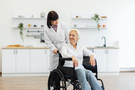 A smiling caregiver pushes an elderly woman in a wheelchair indoors, likely in a kitchen setting,...