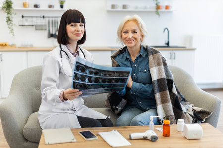 A female doctor shows an older woman her medical scan results while sitting on a sofa. They both smile, indicating a positive interaction.の写真素材