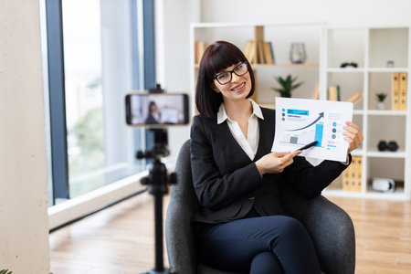 Caucasian woman in thirties presenting business growth report during live video blog recordingの写真素材