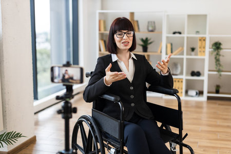 Caucasian woman, young adult, professional attire, sitting wheelchair, speaking camera business-related vlog.の写真素材