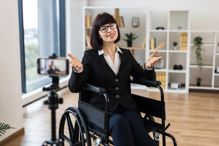 Caucasian woman, young adult, professional attire, sitting wheelchair, speaking camera business-related vlog.の写真素材