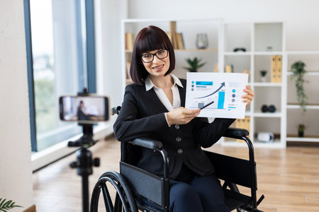 Caucasian woman in professional office showing financial chart during remote video blogging session.の写真素材