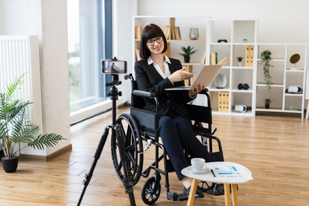 Caucasian woman in wheelchair blogs about business on camera using modern equipment.の写真素材