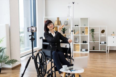 Caucasian woman sitting in wheelchair receiving IV drip and recording business content for vlog...