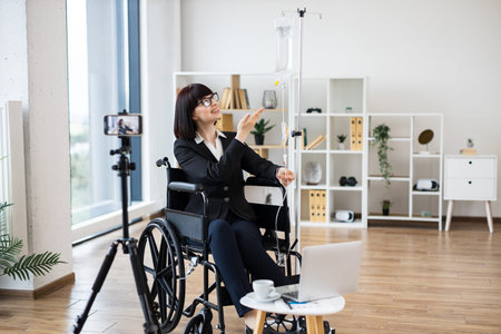 Caucasian woman sitting in wheelchair receiving IV drip and recording business content for vlog...