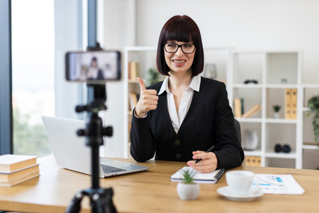 Caucasian woman wearing business attire blogging about professional topics at table with accessories.の写真素材