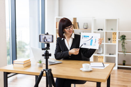 Caucasian woman sitting at table recording blog video about business performance statistics and...