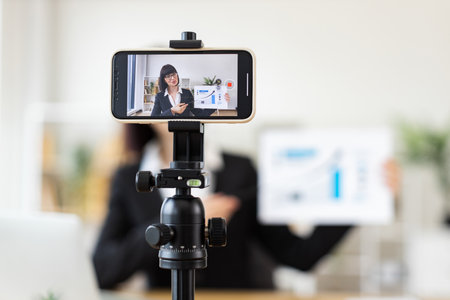 Caucasian young adult woman sitting at table holding presentation while recording blog. Concept of business, communication, and content creation.の写真素材