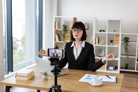 Caucasian woman sitting at desk meditating in office. Professional using self-care during work.
