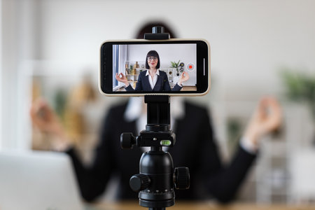 Caucasian adult woman practicing meditation at work, recording session using smartphone and tripod.の写真素材