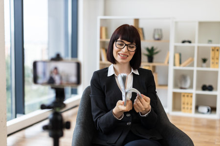 Professional setting with Caucasian adult woman presenting financial concepts through video blogging setup.の写真素材