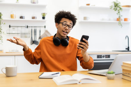A young man with glasses is on a video call, gesturing with his hands while sitting at a table in his kitchen.の写真素材
