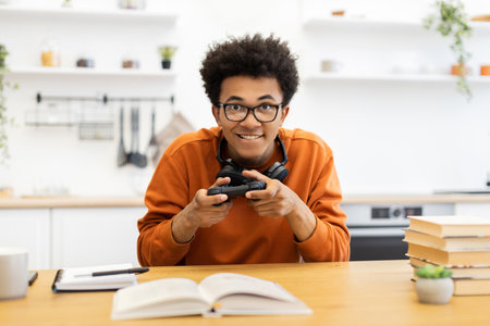 A young man with glasses is playing a video game, holding a controller and smiling at the camera.の写真素材