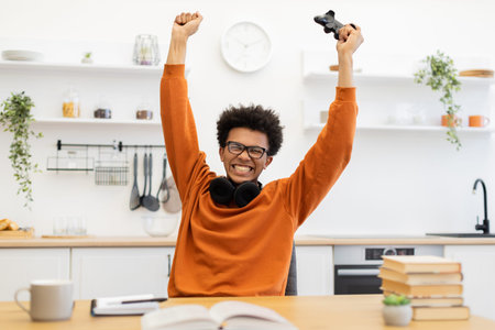 A young man with glasses celebrates a win while playing video games at home, holding a controller.