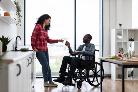 A diverse couple celebrates with wine in a bright, modern kitchen. One partner is in a wheelchair.の写真素材