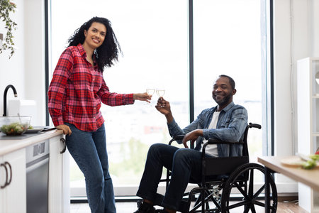 A smiling couple in a modern kitchen toasts with glasses of wine, one person is in a wheelchair.