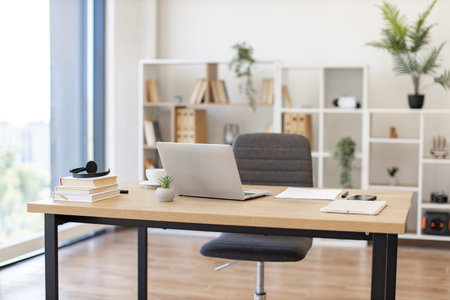 A laptop sits on a wooden desk in a bright, modern office setting, ready for workの写真素材