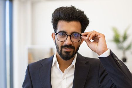 An Indian businessman adjusts his glasses while looking directly at the camera