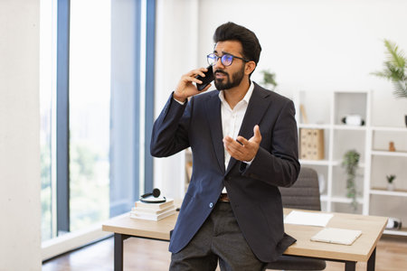 A businessman in a suit is talking on the phone in his office, looking concerned