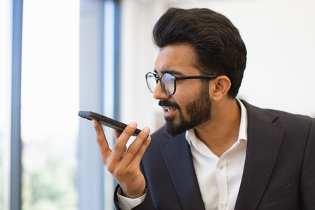 An Indian businessman wearing glasses is talking on his smartphone in an office setting