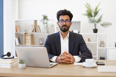 An Indian businessman sits at his desk, looking directly at the camera with a serious expressionの写真素材