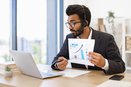 An Arab businessman wearing a headset is presenting a financial report during a video conferenceの写真素材