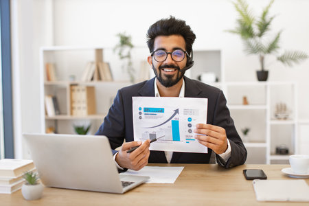 An Indian businessman smiles while presenting a financial report during a video conferenceの写真素材