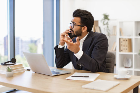 A man in a suit is on a phone call at his desk, looking concernedの写真素材