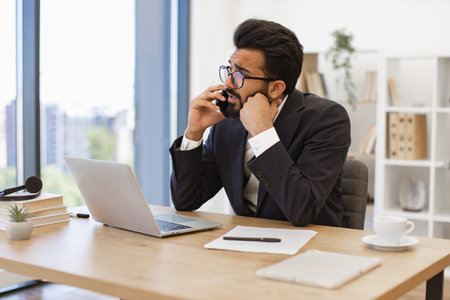 A serious-looking businessman is talking on the phone in his office, looking concernedの写真素材