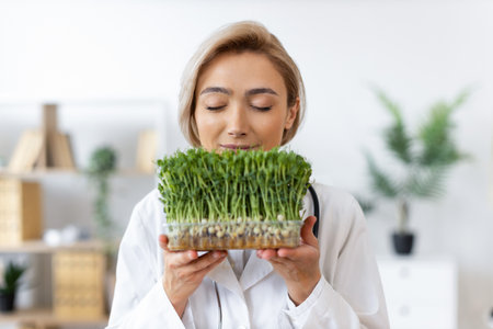 A female doctor in a white coat holds and smells a tray of fresh microgreens, possibly for nutritional assessment.の写真素材
