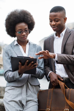 A man and a woman in business attire collaborate outdoors, reviewing documents and engaging in conversationの写真素材