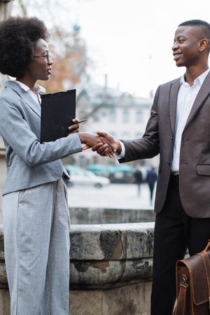 Two professionals, a man and a woman, shake hands outdoors, signifying a successful agreement or partnershipの写真素材