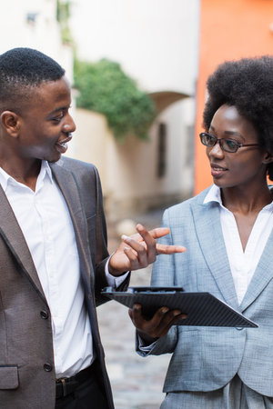 Two professionals in suits discuss a document while standing on a cobblestone street with buildings in the backgroundの写真素材